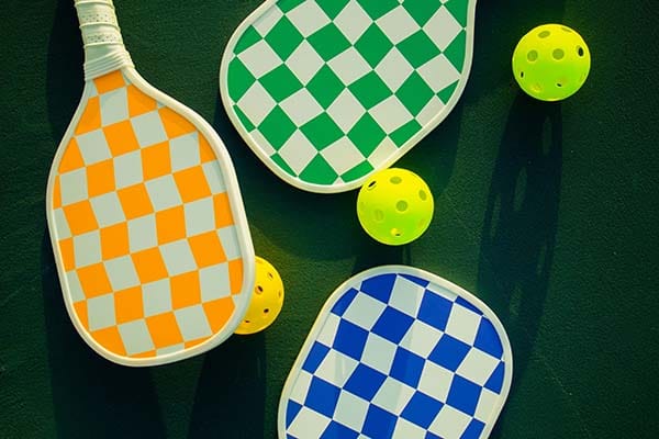 Pickleball-Paddel mit gelben Bällen Pickleball Bälle Unterschiede. Drei bunte Pickleball-Paddel in Orange, Grün und Blau.