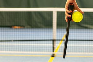 Pickleball Paddle und gelber Ball vor dem Netz – Pickleball Guides zu den Spielregeln. Symbolbild