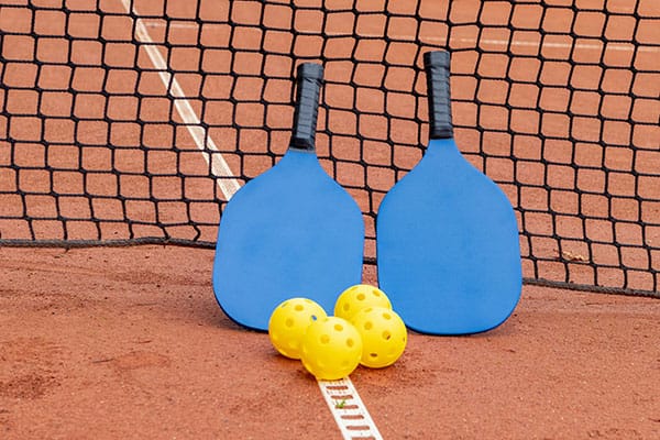 Pickleball lernen für Anfänger – Ausrüstung auf dem Platz Zwei blaue Pickleball Schläger und mehrere Bälle auf dem Platz – ideal für Anfänger, die Pickleball lernen wollen.